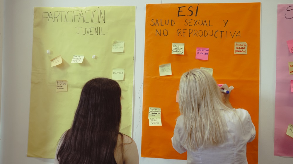 Dos chicas pegando papeles en un afiche