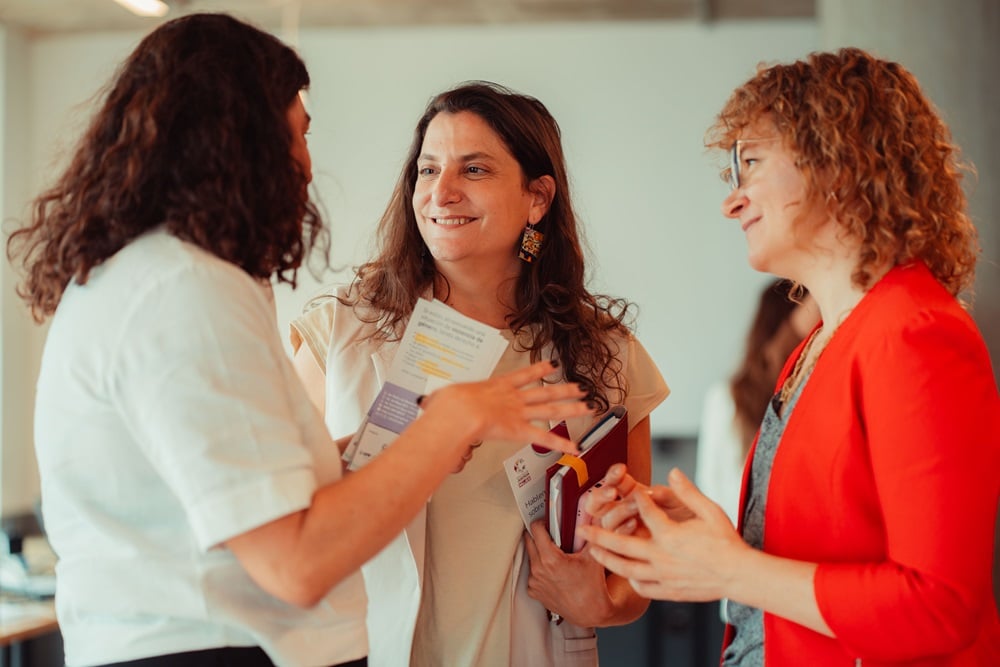 Tres mujeres conversan en el evento. Una habla y las otras dos la escuchan atentamente.