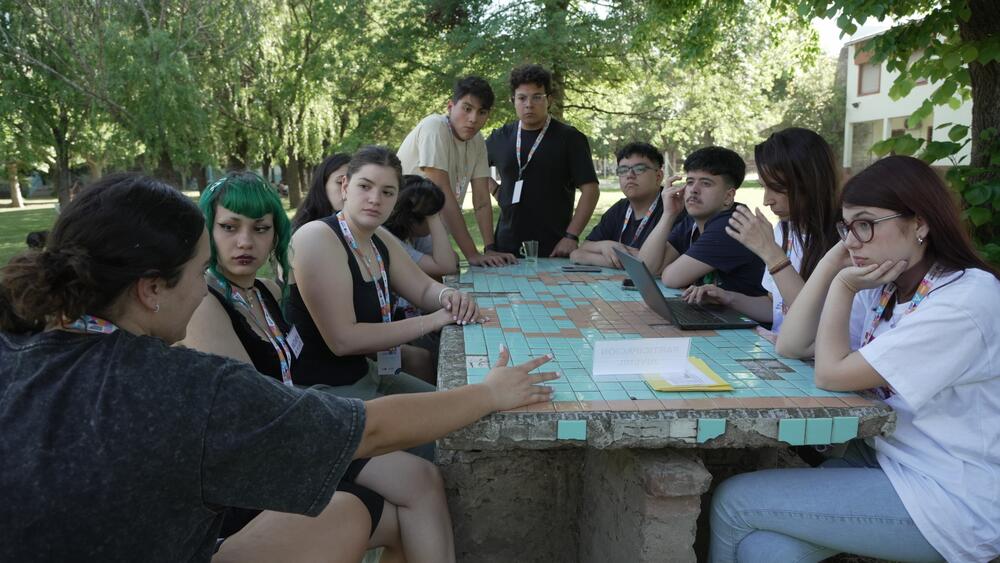 Un grupo de jóvenes, en su mayoría mujeres, debate alrededor de una mesa en un parque