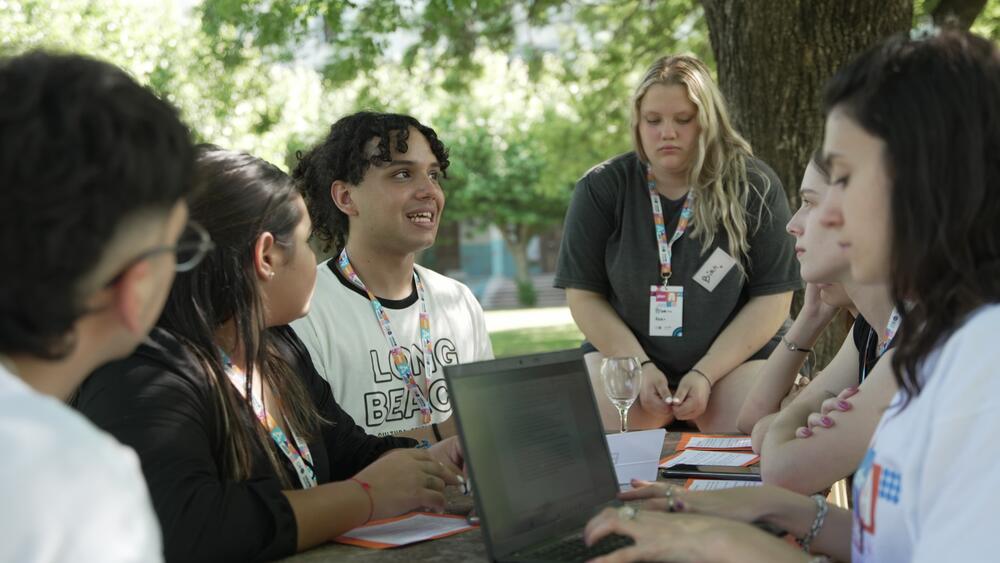 Jóvenes intercambian sobre uno de los ejes de Plan A en un espacio abierto, con plantas. Una de las jóvenes toma nota en una computadora.