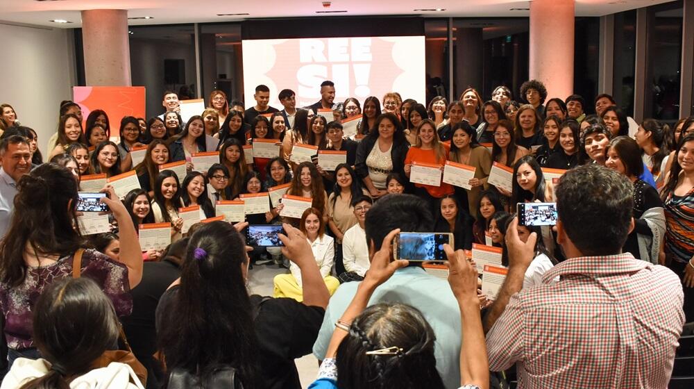 Un gran grupo de personas sostienen certificados tras el proyecto REE-Sí y otro grupo les saca fotos con teléfonos celulares