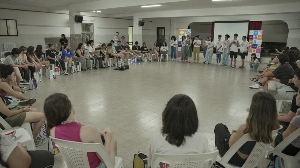 Grupo de adolescentes y jóvenes sentados en ronda en un salón amplio.