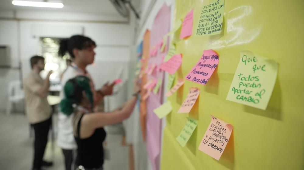 Jóvenes pegando papales con frases en afiches pegados sobre una pared.