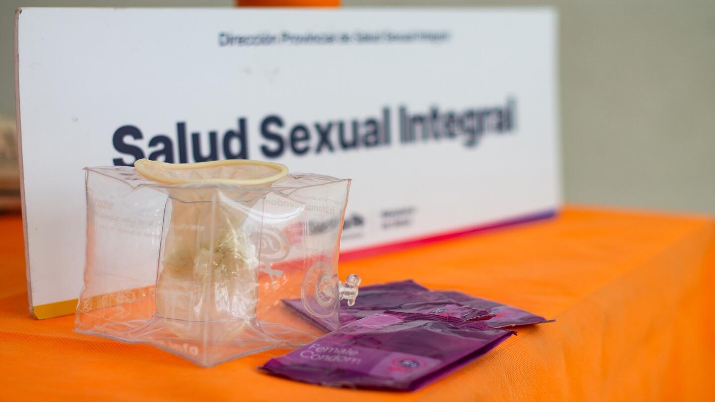 Un preservativo vaginal y su empaque. Atrás un cartel dice salud sexual integral