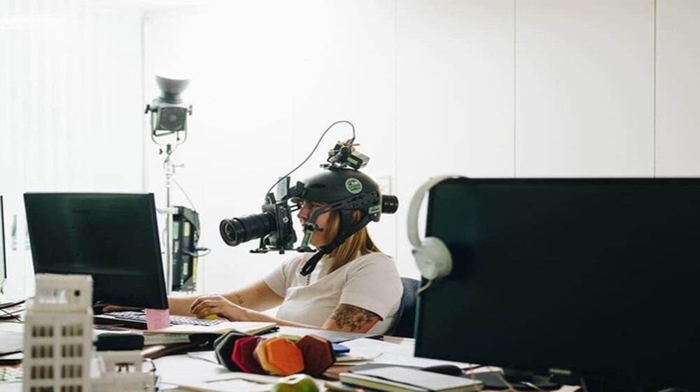 Una joven con un casco y una cámara, sentada frente a una computadora